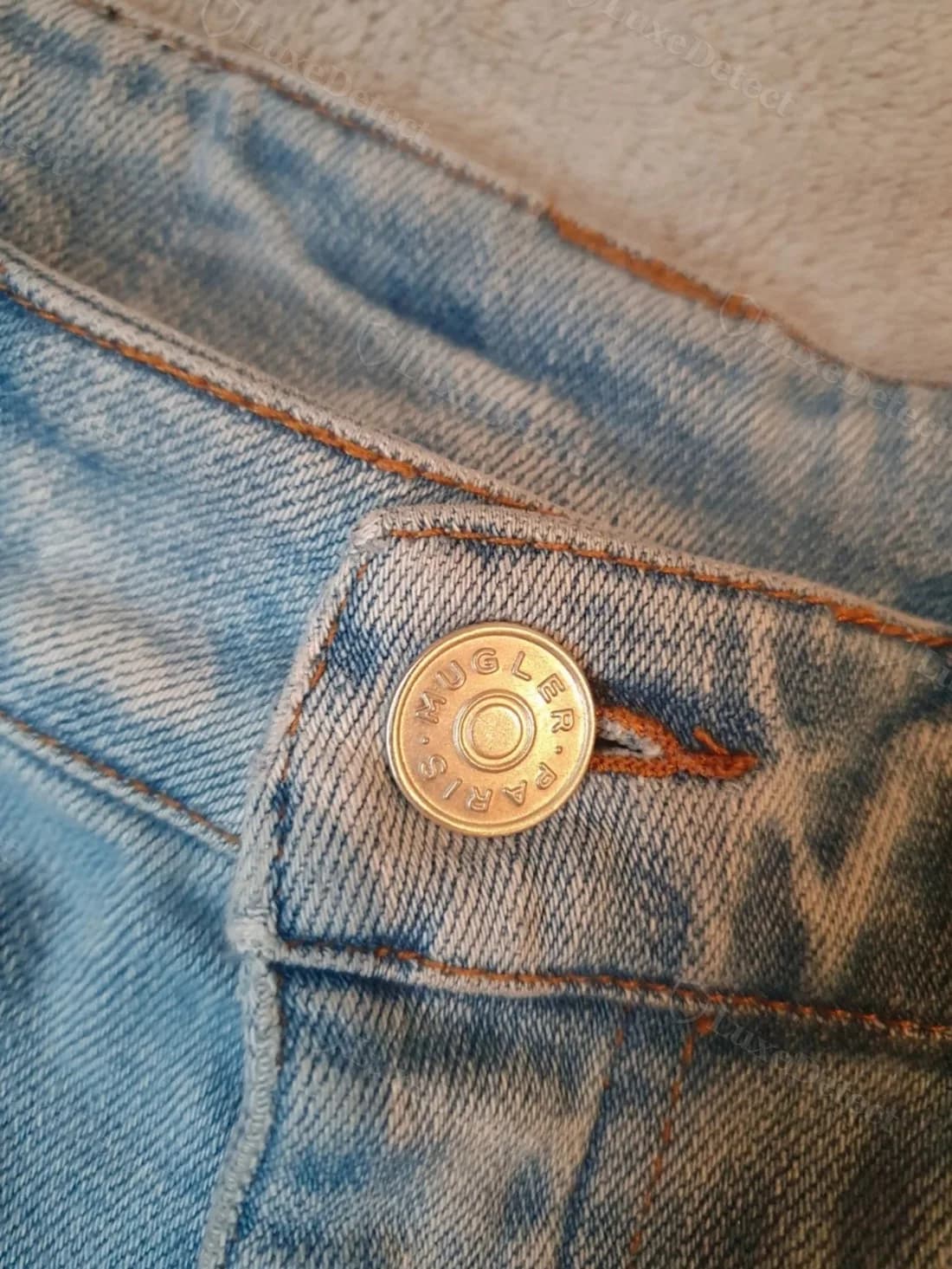 Authentic denim rivet button stamped "MUGLER · PARIS" in a circle, brass finish, on confirmed-authentic curved-seam jeans.