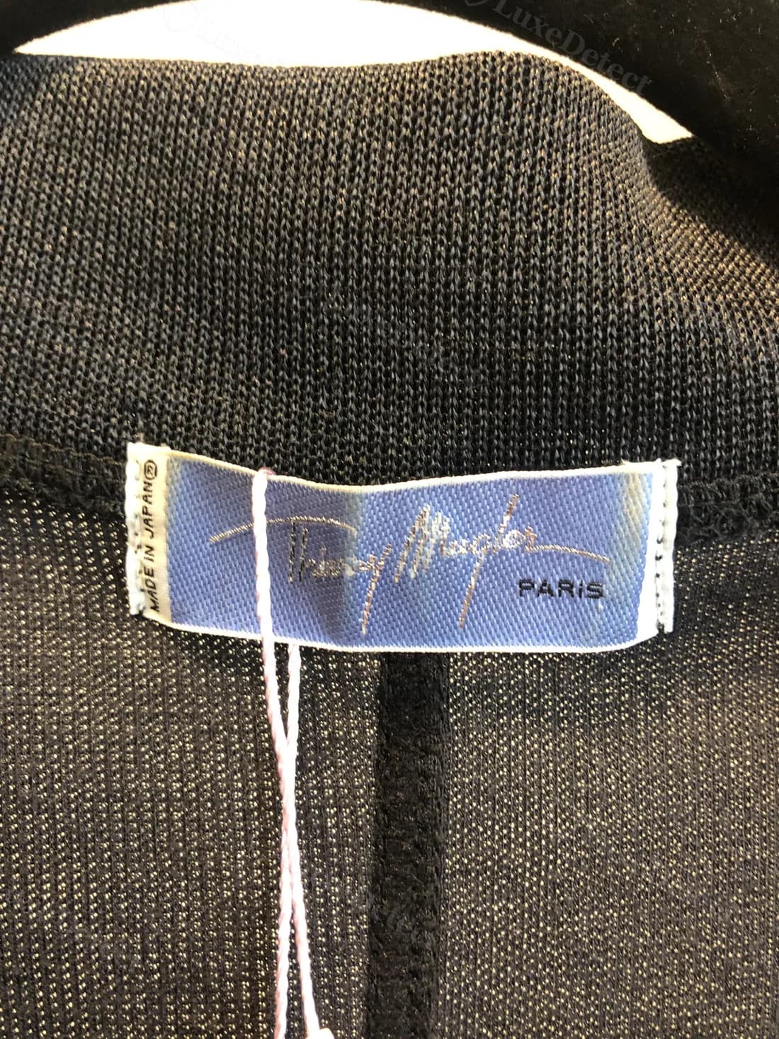 Interior label from a confirmed counterfeit garment: lighter periwinkle satin, sewn flat at both ends, signature in a warmer gold thread, with an extra "Made in Japan" tag stitched to the edge.