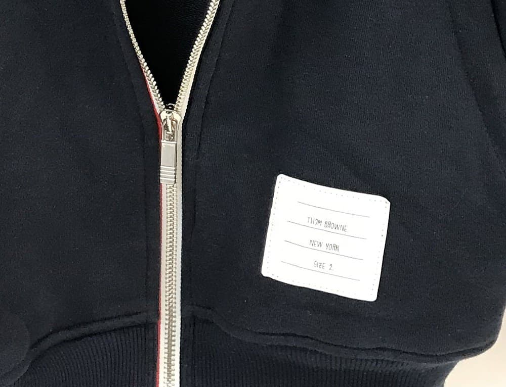 Genuine Thom Browne interior placket tag — a printed white patch reading "THOM BROWNE," "NEW YORK," and the size, next to the tricolor grosgrain trim