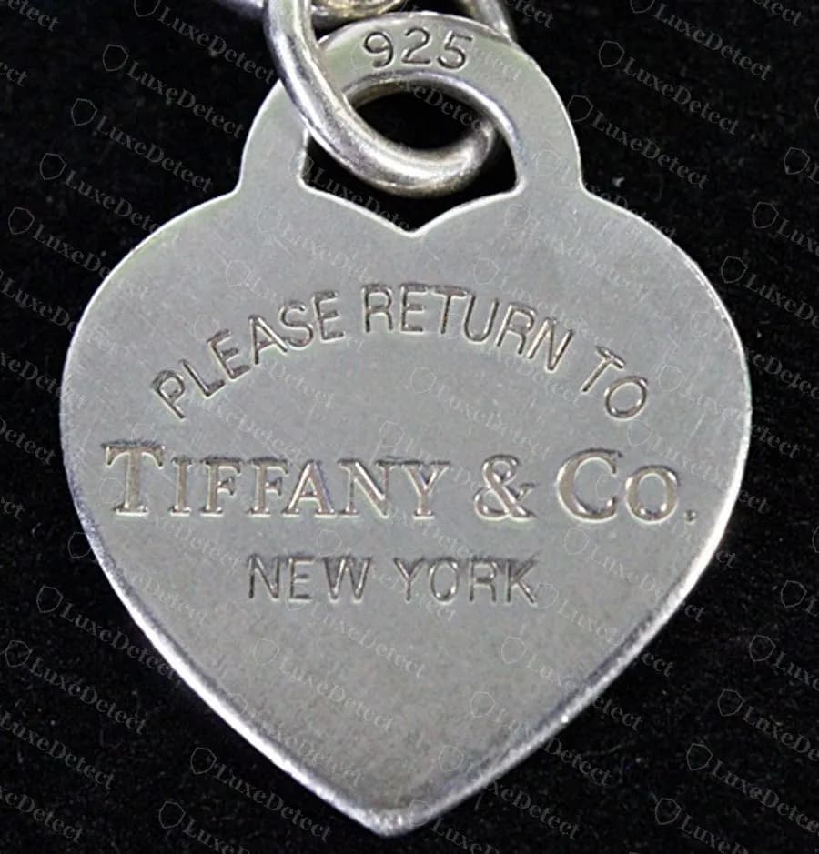 Targhetta a cuore Return to Tiffany originale: PLEASE RETURN TO in un unico arco regolare con uno spazio netto tra le parole, TIFFANY & CO. in maiuscole serif, NEW YORK sotto e 925 punzonato sul fronte dell’anellino