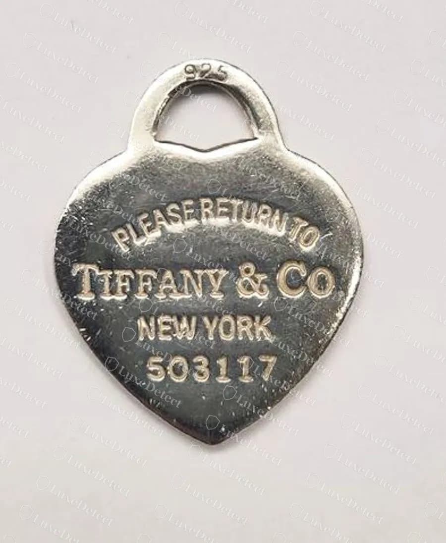 Gefälschter Herz-Anhänger mit einer Nummer unter NEW YORK an derselben Stelle wie eine echte Registriernummer; beachten Sie das zusammengedrängte PLEASERETURNTO