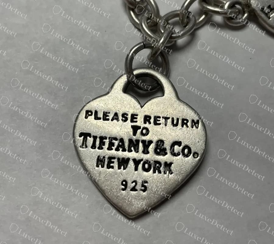 Targhetta a cuore contraffatta: PLEASE RETURN su una riga dritta con TO su una seconda riga, invece di un unico arco sulla parte alta del cuore