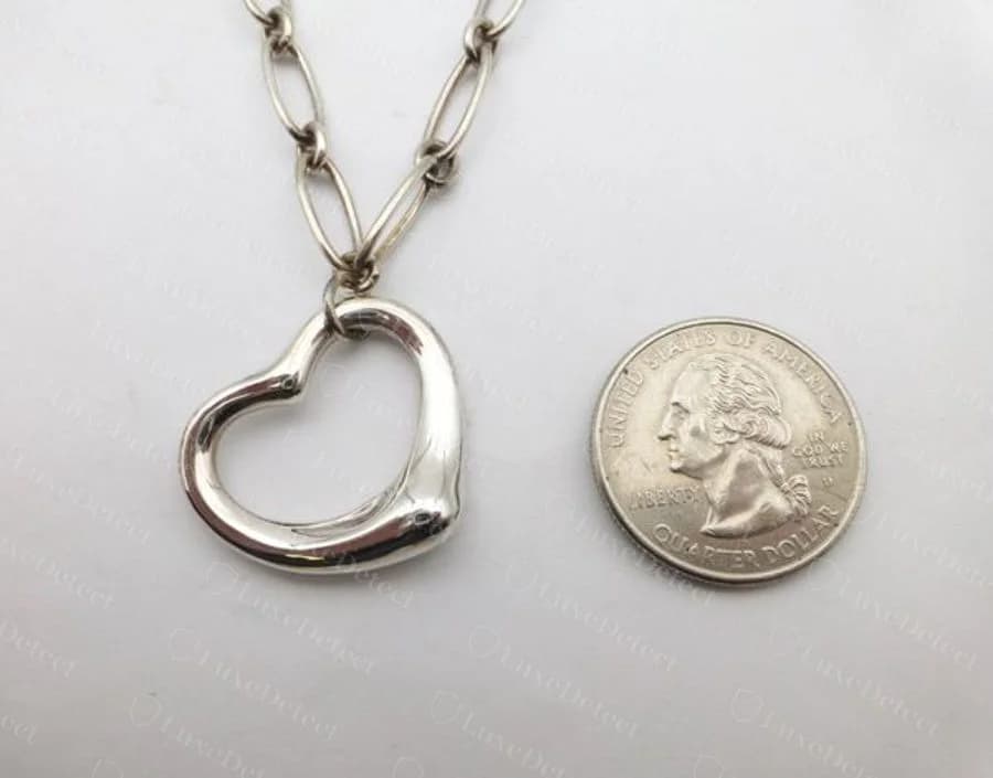Counterfeit Elsa Peretti Open Heart necklace photographed against a US quarter, the pendant reading at the coin's diameter and hanging from a chunky oval-link chain instead of a fine cable chain