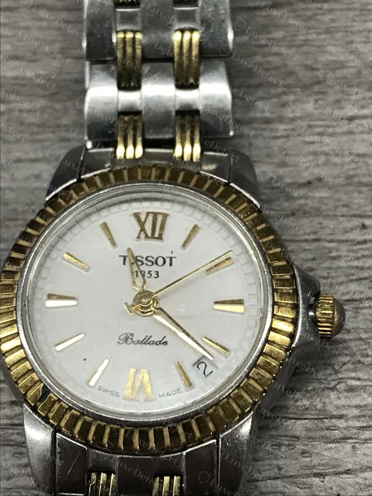Un Tissot Ballade de señora original, bicolor: TISSOT 1853 bajo las 12, la palabra en cursiva Ballade más abajo en la esfera, una ventana de fecha, un bisel estriado de tono dorado y SWISS MADE en la parte inferior.