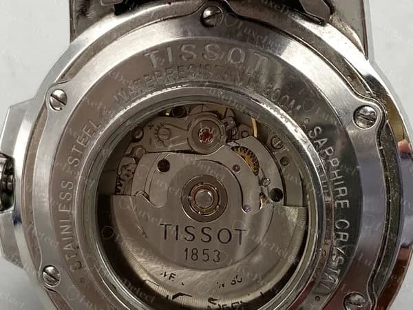 Fondo de un Tissot Seastar 1000 automático original: un aro roscado que dice STAINLESS STEEL, SAPPHIRE CRYSTAL y una clasificación de resistencia al agua alrededor de una ventana de exhibición, con TISSOT 1853 impreso en el rotor.