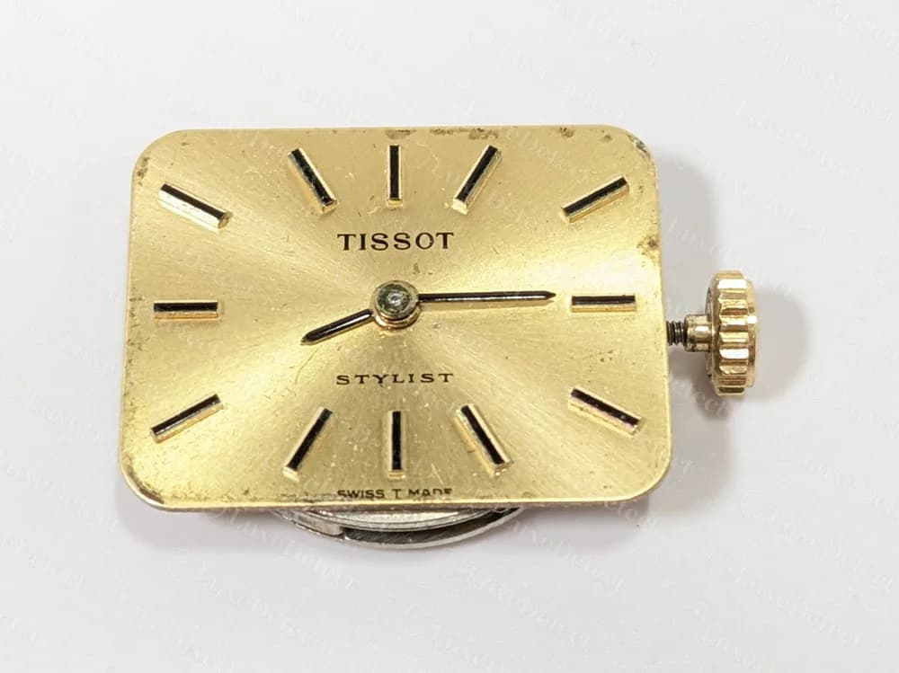 Movimento e mostrador de um Tissot Stylist vintage: mostrador dourado com índices em bastão, com TISSOT acima de STYLIST, SWISS T MADE impresso na borda inferior e sem 1853 no mostrador.