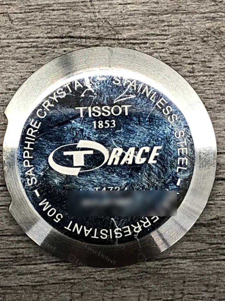 Fundo da caixa de um Tissot T-Race original: TISSOT 1853 acima do logo T-RACE, SAPPHIRE CRYSTAL e STAINLESS STEEL ao redor da borda e WATERRESISTANT 50M sem hífen.