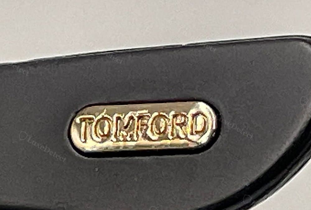Gefälschte „T“-Plakette – schief, ungleichmäßiger, klecksiger Schriftzug mit uneinheitlicher Buchstabenstärke und einem verzogenen „O“