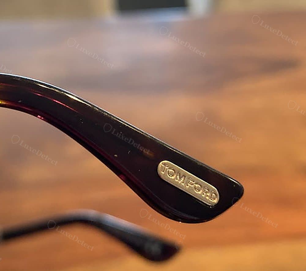 Authentic Tom Ford "T" plaque — flush metal oval, clean even serif "TOMFORD" lettering, sharp edges