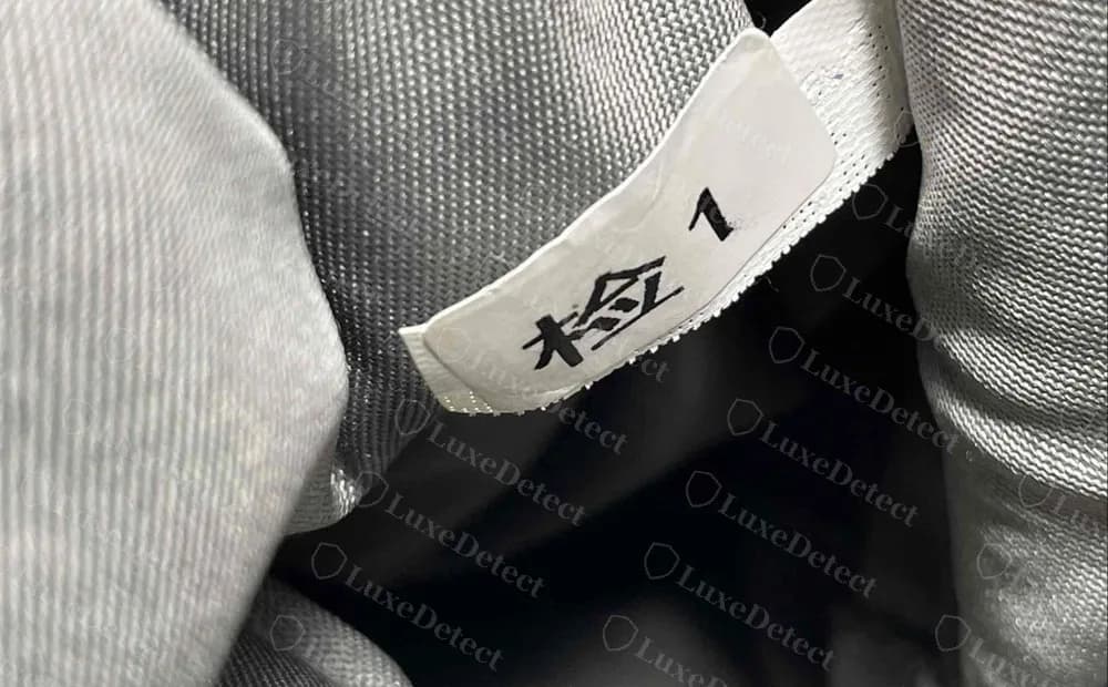 Forro de un bolso Tory Burch falso: pequeña etiqueta blanca impresa con el carácter chino 检 y el número 1, cosida en el interior gris