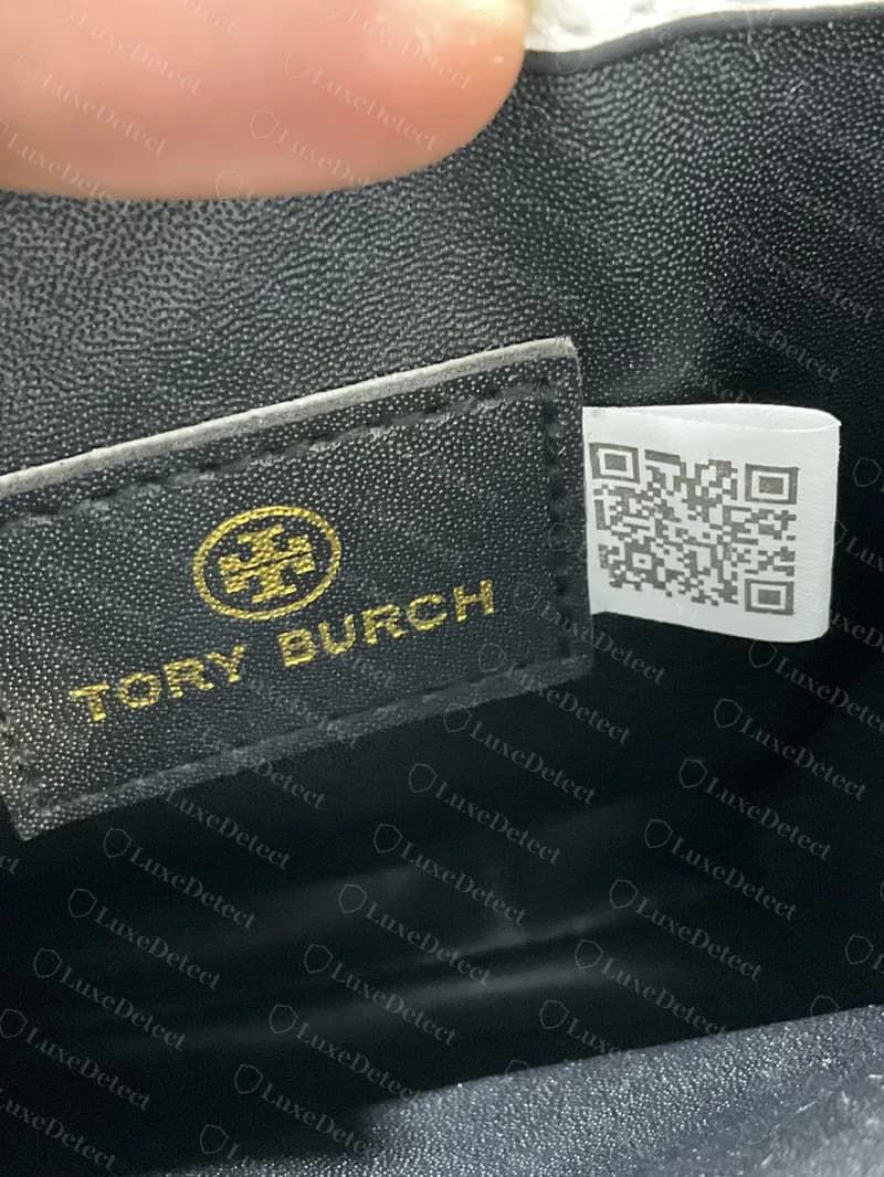 Interior de un bolso Tory Burch falso: una etiqueta de tela blanca impresa con un código QR, cosida junto a un parche de forro negro estampado con TORY BURCH y la Double T en dorado