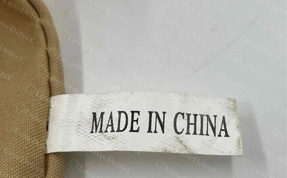 Bandolera Tory Burch falsa: cinta blanca estrecha que dice MADE IN CHINA en una tipografía con serifas estilo Times, sin línea de código