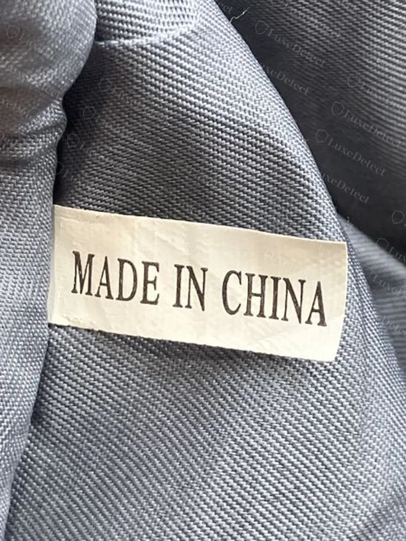 Forro de un bolso Tory Burch falso: cinta crema con mayúsculas con serifas MADE IN CHINA y sin código de estilo ni fecha, cosida dentro de un forro gris azulado