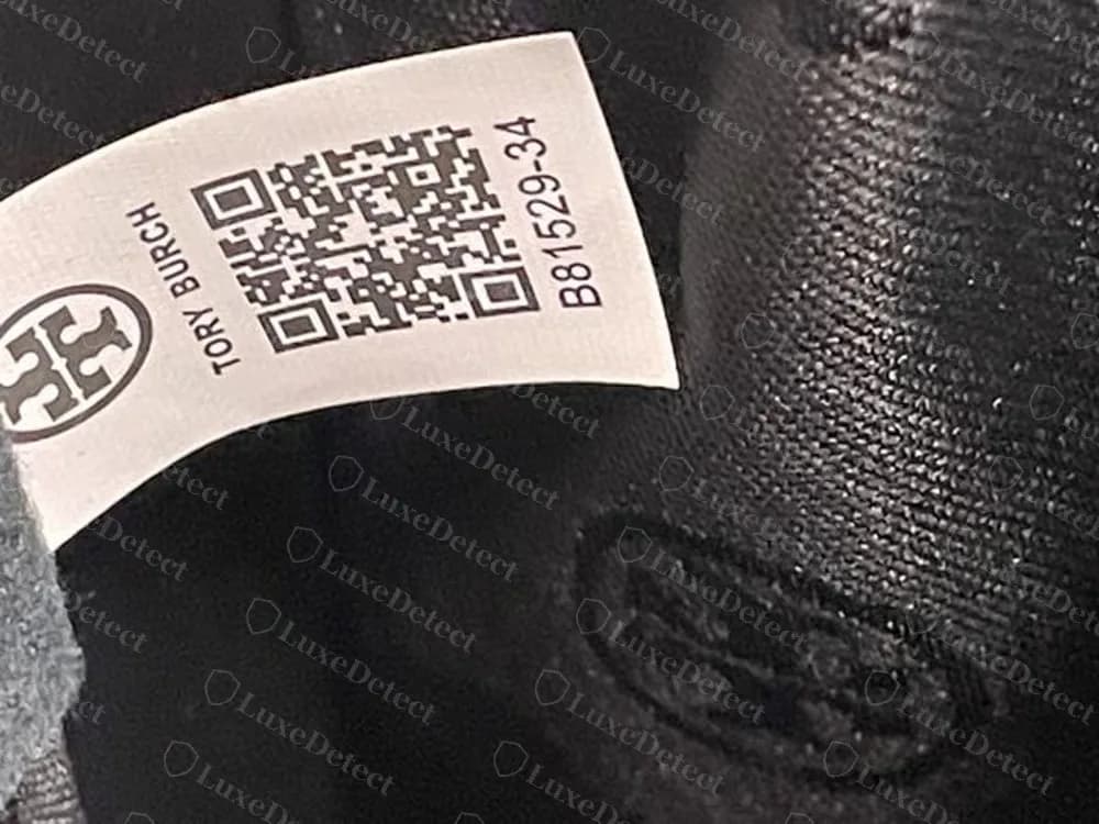 Interior de un bolso Tory Burch falso: etiqueta blanca impresa con la Double T, TORY BURCH, un código QR y el número B81529-34, cosida dentro de un forro negro