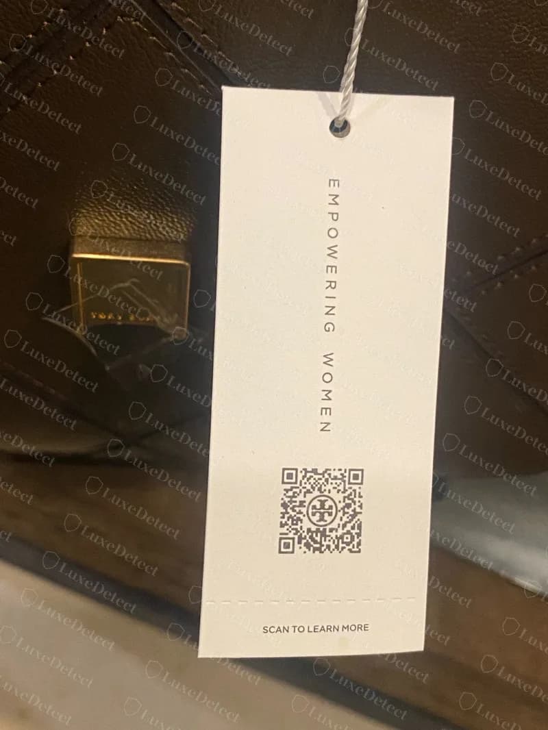 Echte Tory Burch Hangkarte aus Papier an einer Schnur mit EMPOWERING WOMEN, einem QR-Code und SCAN TO LEARN MORE, hängend im Inneren einer braunen Ledertasche