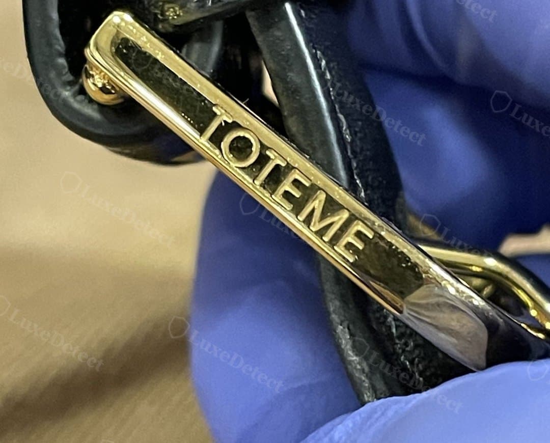 Counterfeit T-Lock clasp: gold-tone hardware with "TOTEME" engraved directly into the crossbar face — the genuine T-Lock hardware we have seen carries no branding