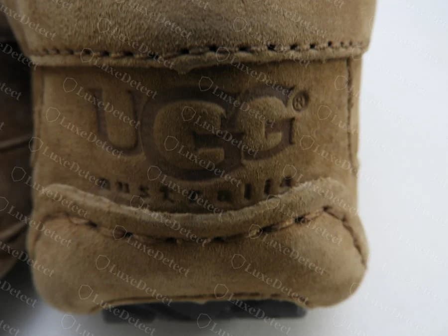 Genuine UGG suede-embossed heel patch: UGG australia debossed directly into the suede at the heel of a moccasin-style slipper, framed by a stitched seam above and below