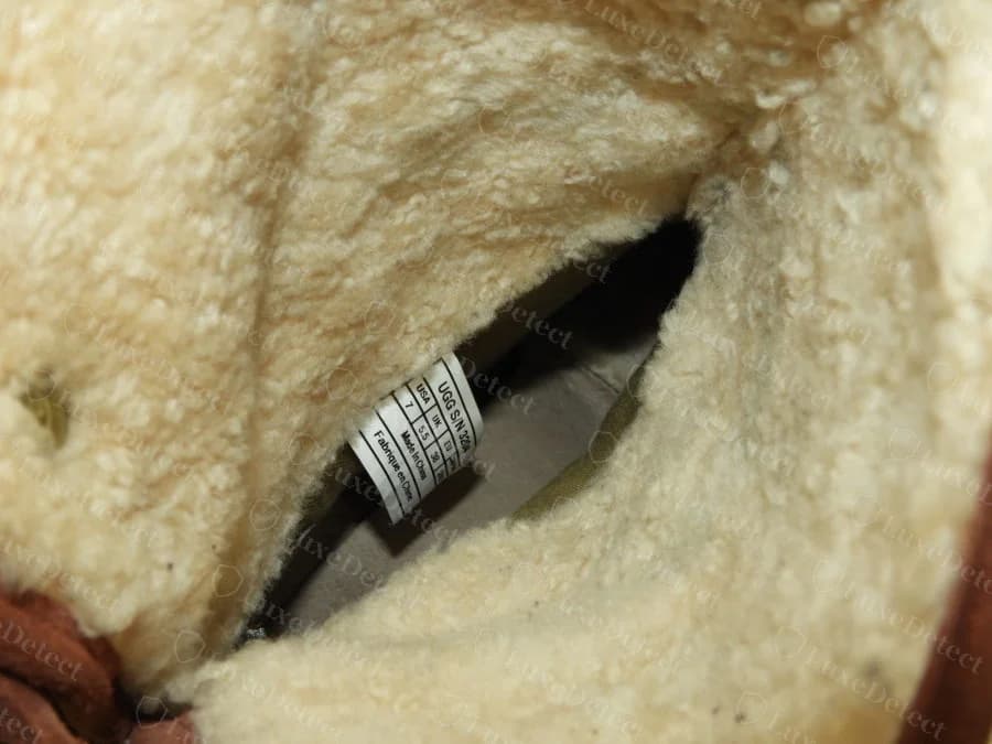 Genuine UGG interior fabric tag reading UGG S/N followed by a four-digit number, a USA/UK/EU/Japan size conversion table, and Made In China with the French equivalent Fabrique en Chine, stitched into the sheepskin lining