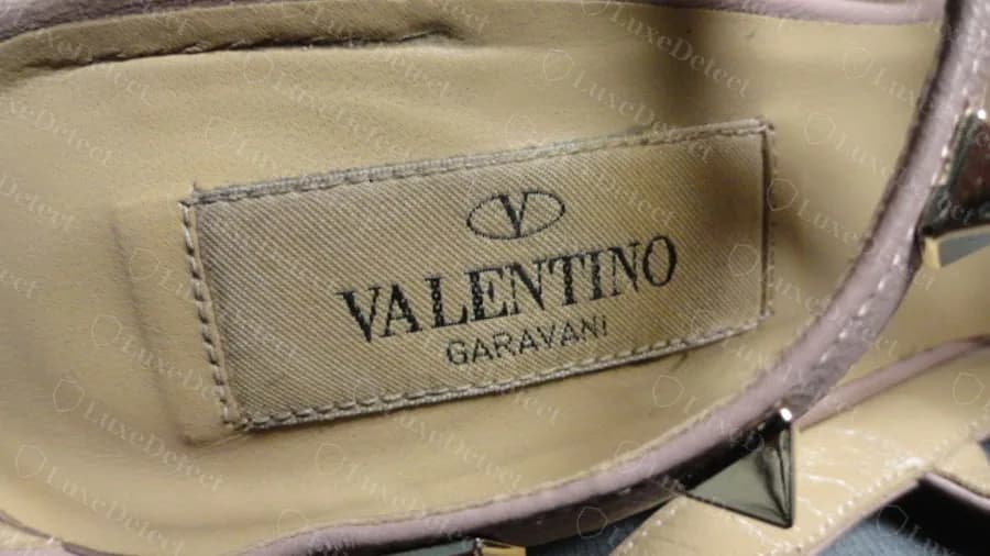 Insole label on a genuine Rockstud pump, the V logo above VALENTINO GARAVANI on a stitched cloth patch, slightly worn from use
