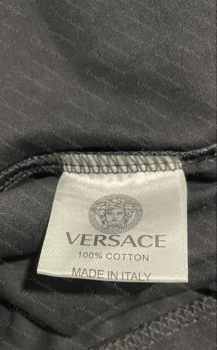 Camiseta Versace falsificada: etiqueta blanca corta con una Medusa gris redonda, VERSACE, 100% COTTON y MADE IN ITALY, sin dirección ni código