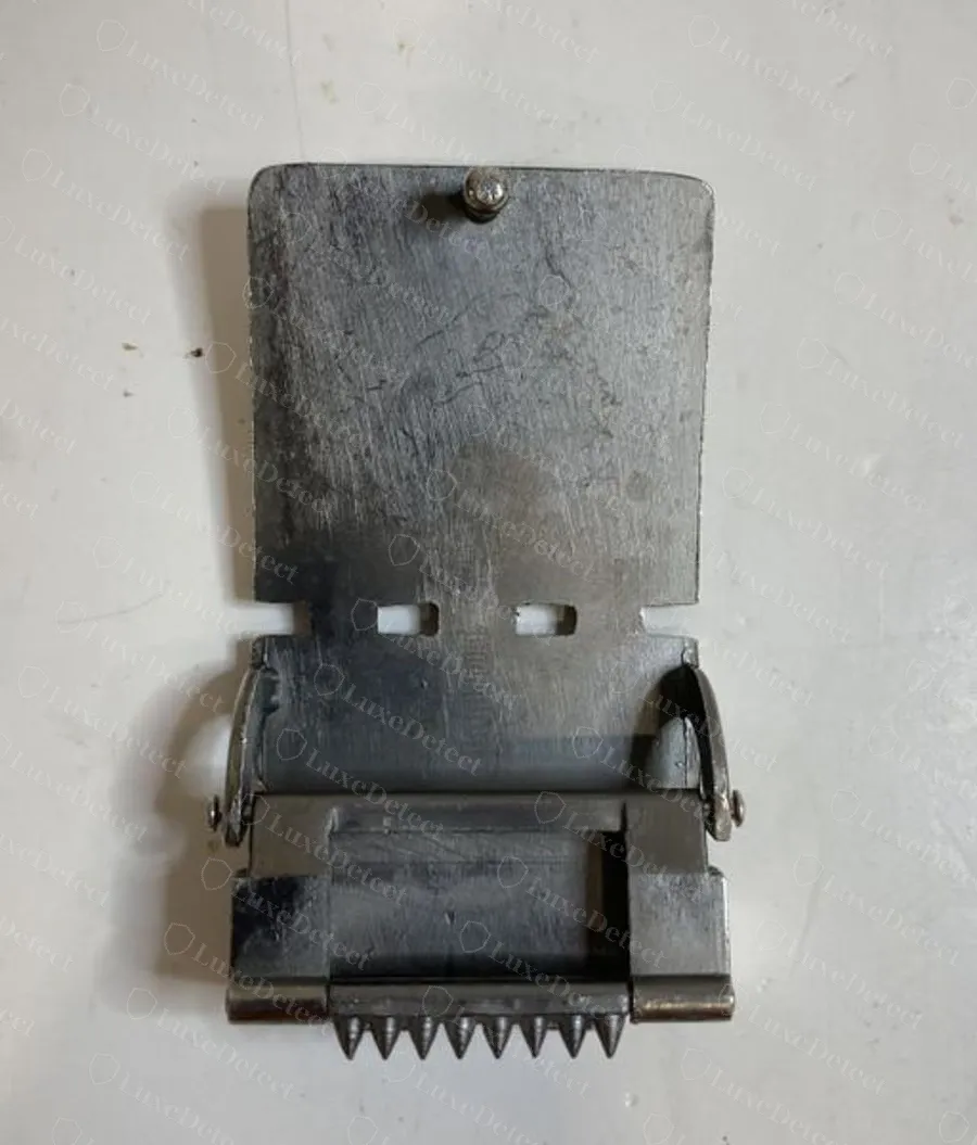 Hebilla de trinquete dictaminada como falsa, abierta para mostrar la pinza dentada y la placa de metal lisa