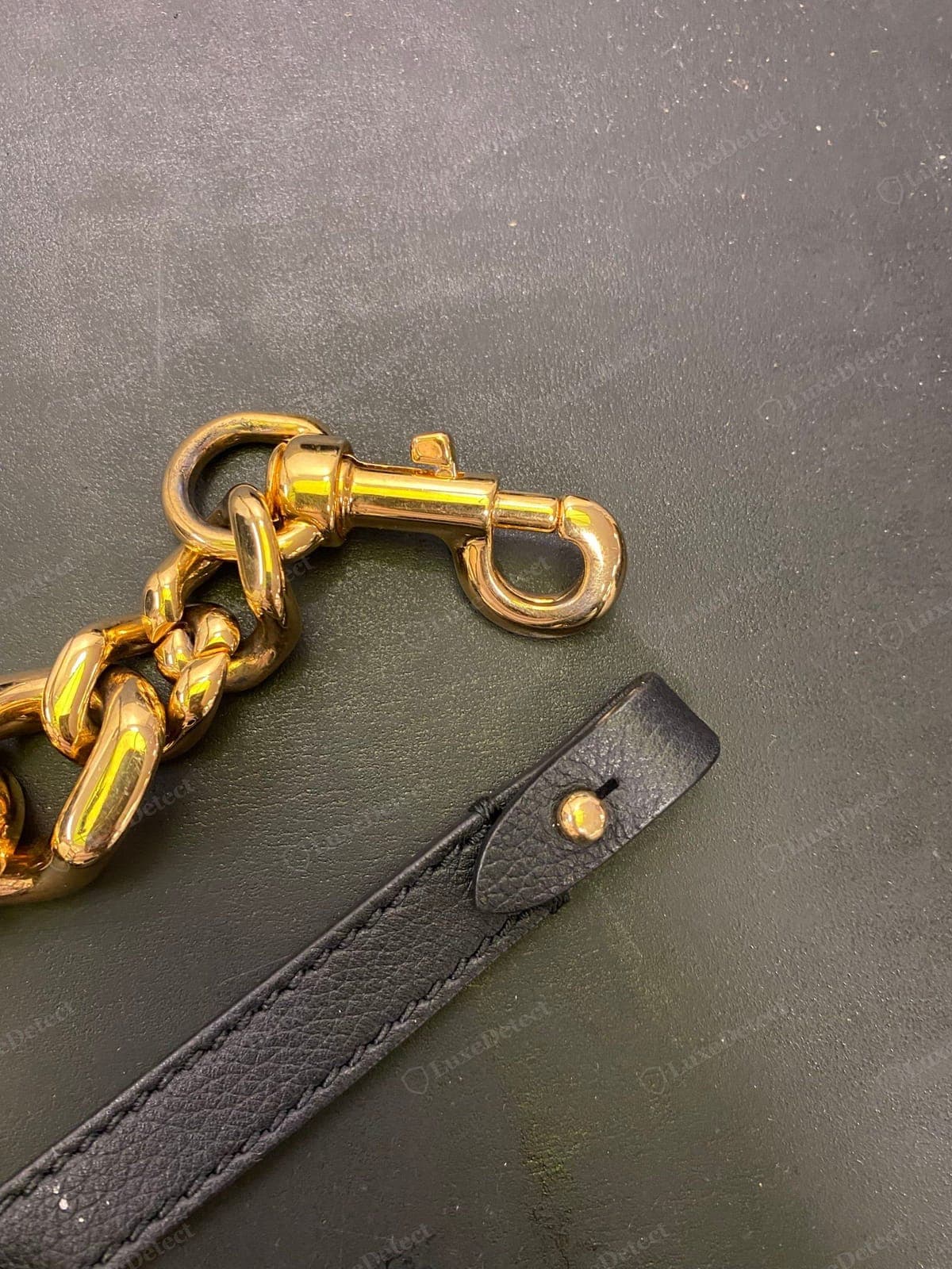 Herrajes de cadena genuinos de un Versace La Medusa — una correa de eslabones dorada maciza y un mosquetón pesado de fundición sin costuras, unidos a una lengüeta de correa de cuero granulado negro con un remache dorado