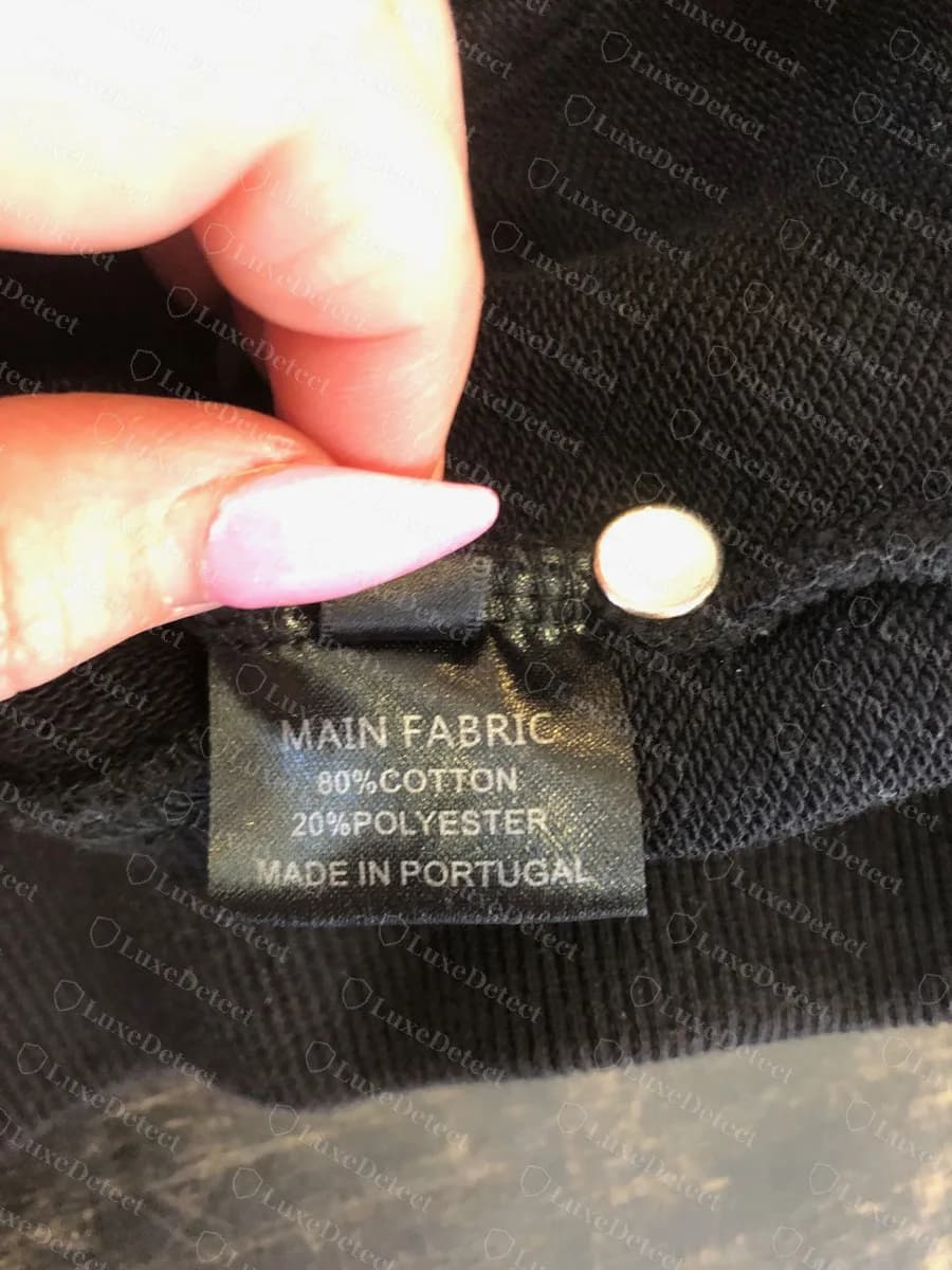 Genuine Vetements black woven composition label reading MAIN FABRIC 80% COTTON 20% POLYESTER and MADE IN PORTUGAL, with a small folded tab above it, inside a black hoodie
