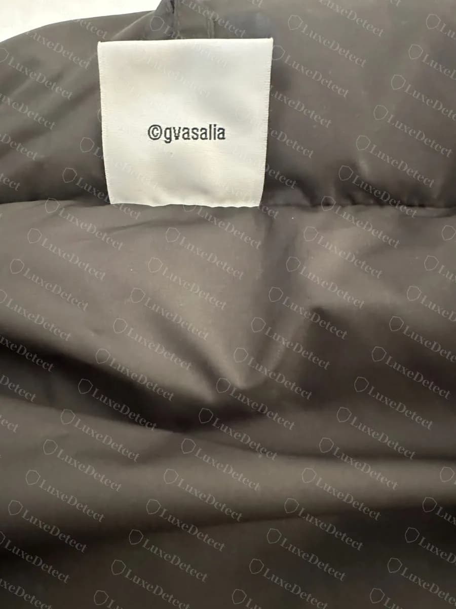 Genuine plain white tag embroidered with the lowercase text ©gvasalia, sewn inside the neck of a black puffer jacket