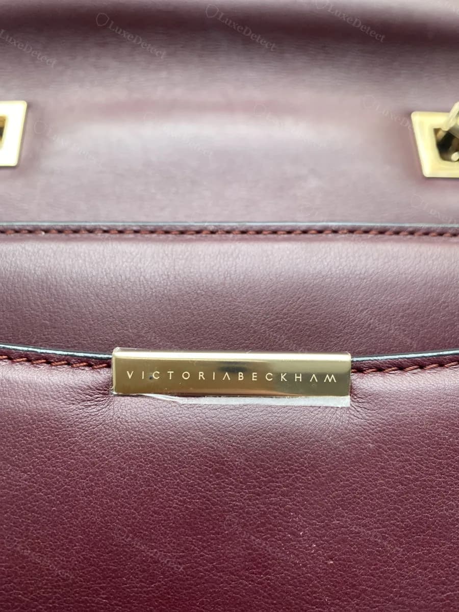 Genuine Victoria Beckham logo bar engraved into the leather beside a hexagonal chain closure, wordmark run together with no space