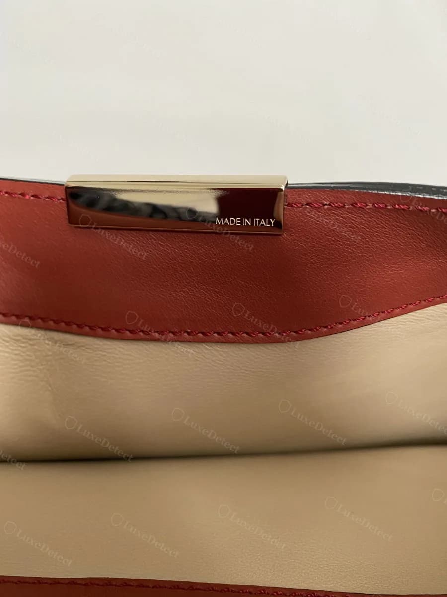 Genuine Victoria Beckham hardware bar engraved "MADE IN ITALY," mounted flush against tricolor leather panelling near the flap's top edge