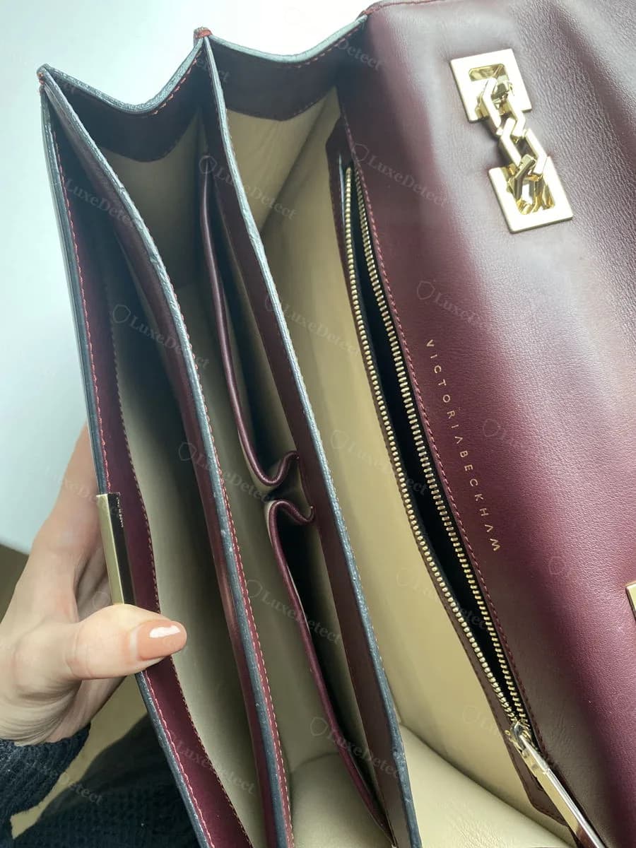 Interior of a genuine Victoria Beckham bag showing card compartments, an interior zip pocket with the wordmark stamped beside the zipper, and the hexagonal closure hardware visible from inside