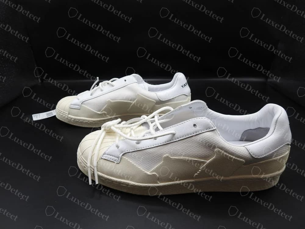 Pestañas del talón de unas Y-3 Super Takusan originales con YOHJI YAMAMOTO en negro sobre cuero blanco, sobre una suela cupsole color crema, con una etiqueta colgante negra