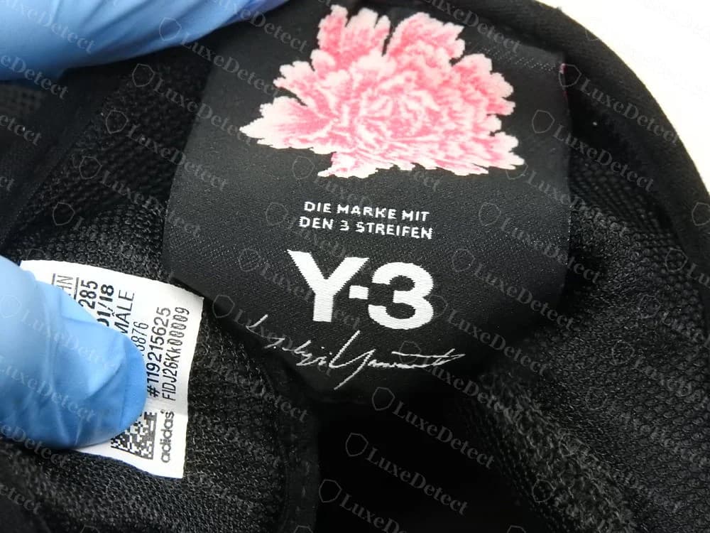 Etiqueta de la lengüeta de unas Y-3 originales en una zapatilla estilo baloncesto James Harden BYW, con una estampa de flor rosa, las palabras DIE MARKE MIT DEN 3 STREIFEN, el logo de Y-3 y una firma de estilo manuscrito