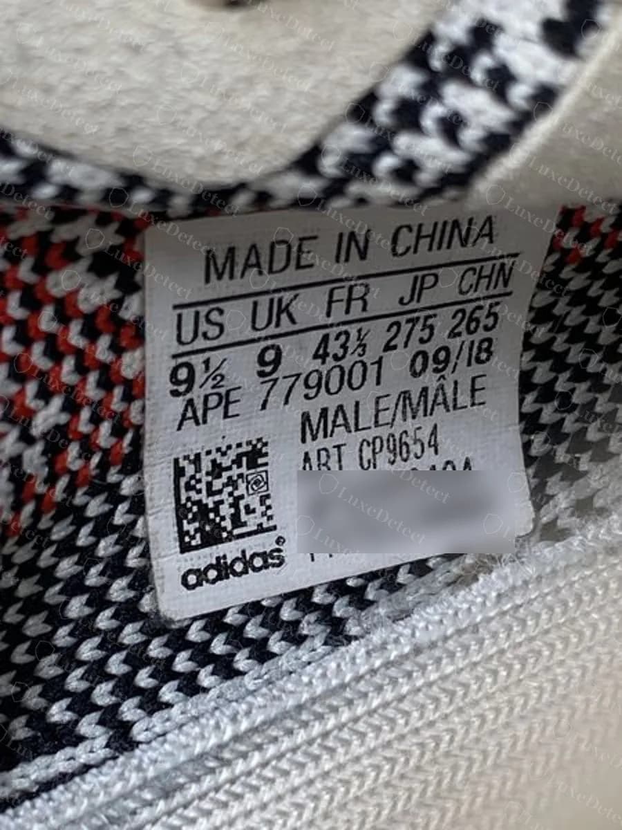 Echtes Größenetikett eines Zebra (CP9654): MADE IN CHINA, ein Raster mit fünf Spalten US UK FR JP CHN, Fabrikcode APE 779001 mit dem Datum 09/18, MALE/MÂLE, die ART-Nummer, ein Data-Matrix-Code und das adidas-Logo; die Seriennummernzeilen des Exemplars sind unkenntlich gemacht
