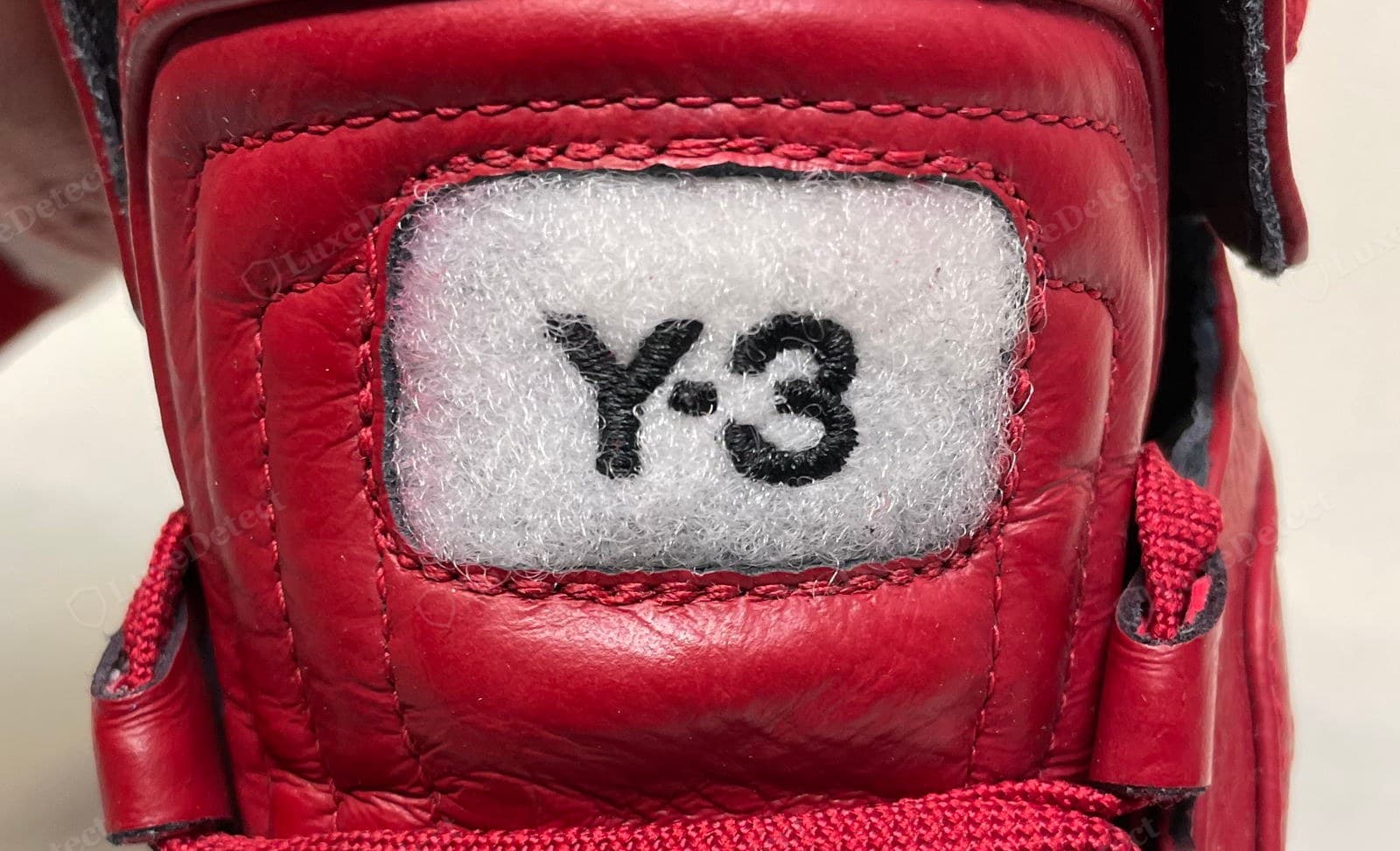 Counterfeit Y-3 sneaker heel tab — the "Y-3" embroidered onto a fuzzy white patch with lumpy stitching and slightly irregular letterforms, the "3" too heavy