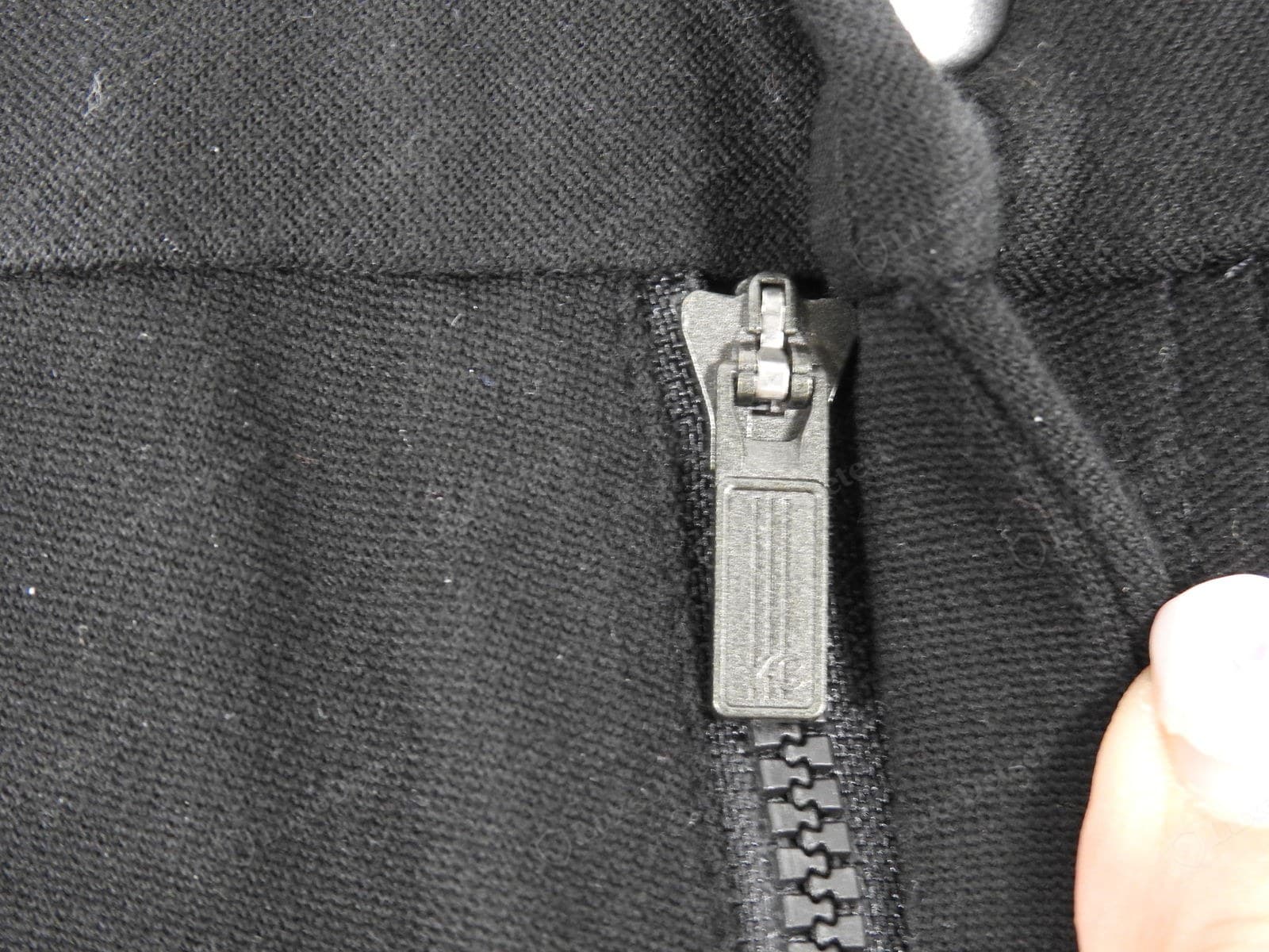 Genuine Yohji Yamamoto zip — a moulded matte-black pull on a chunky plastic-tooth zip, the maker's mark cleanly embossed on the tab, set into a dense black wool seam